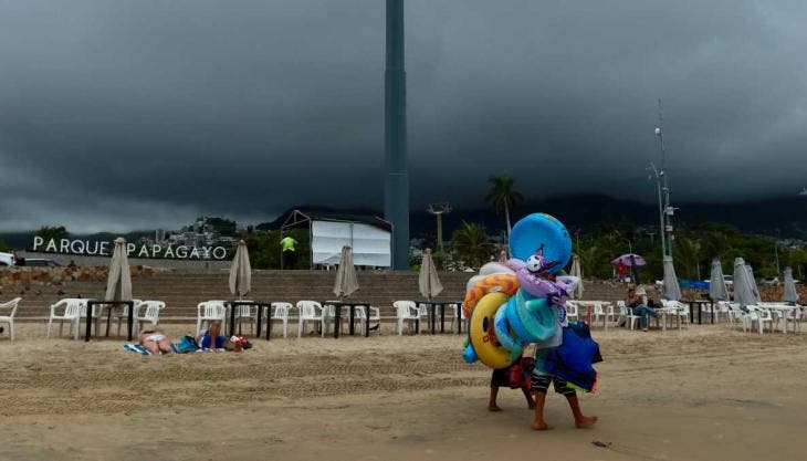 Vendedores caminan en una playa de Acapulco