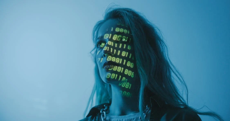 Mujer observando una pantalla que refleja en su rostro una secuencia de ceros y unos, simbolizando la interacción con la tecnología y el mundo digital.