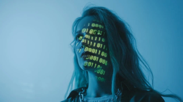 Mujer observando una pantalla que refleja en su rostro una secuencia de ceros y unos, simbolizando la interacción con la tecnología y el mundo digital.