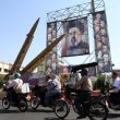 Unos iraníes pasan en coche junto a misiles iraníes Zolfaghar colocados frente a una valla publicitaria con la imagen del líder supremo de Irán, el ayatolá Mojtaba Jameneí (Foto EFE)