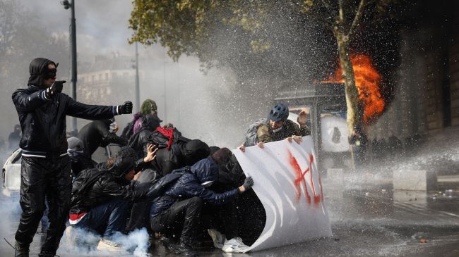 Los manifestantes se resguardan tras una pancarta con la inscripción "ACAB" mientras la policía francesa utiliza un cañón de agua tras los enfrentamientos ocurridos durante una manifestación contra el aumento del coste de la vida y los recortes en los servicios públicos en París, Francia. Los manifestantes se resguardan tras una pancarta con la inscripción "ACAB" mientras la policía francesa utiliza un cañón de agua tras los enfrentamientos ocurridos durante una manifestación contra el aumento del coste de la vida y los recortes en los servicios públicos en París, Francia.