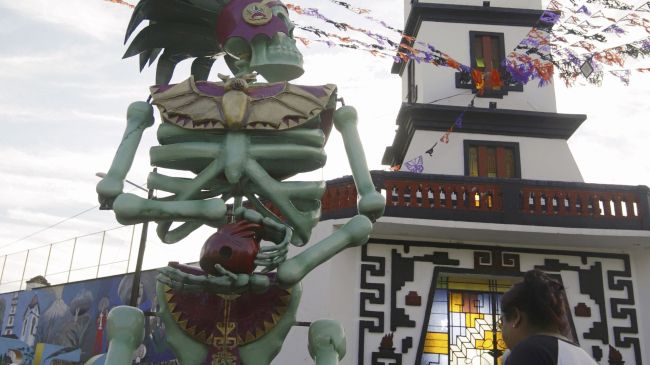 Una persona observa una catrina monumental entre los atractivos del Día de Muertos en Atlixco, Puebla (México). Las figuras, inspiradas en dioses prehispánicos, adornan campos de cempasúchil, plazas y calles del municipio. EFE/ Hilda Ríos